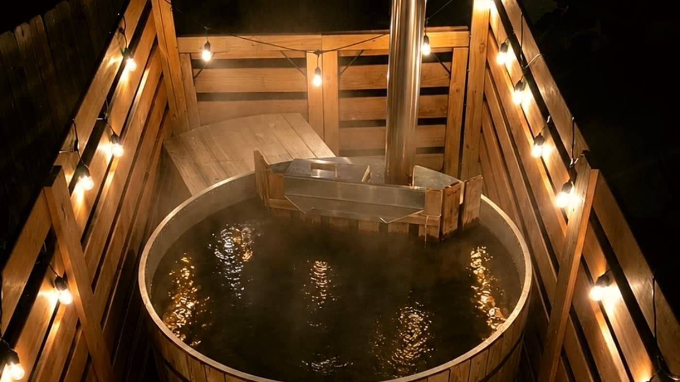 Aerial view of the steaming cedar hot tub at dusk with string lights